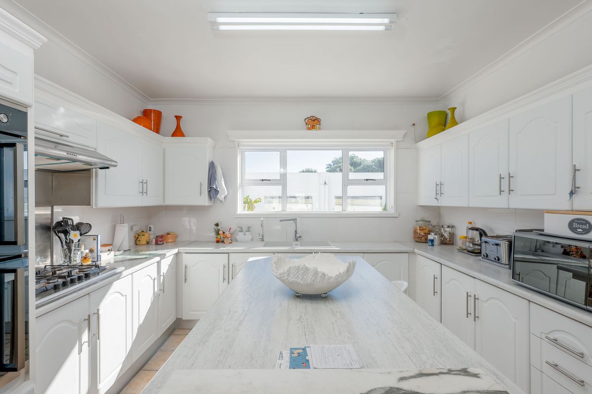 A bright, well-maintained kitchen featuring white cabinetry, a central island, built-in oven, gas hob, and ample counter space with a functional layout.