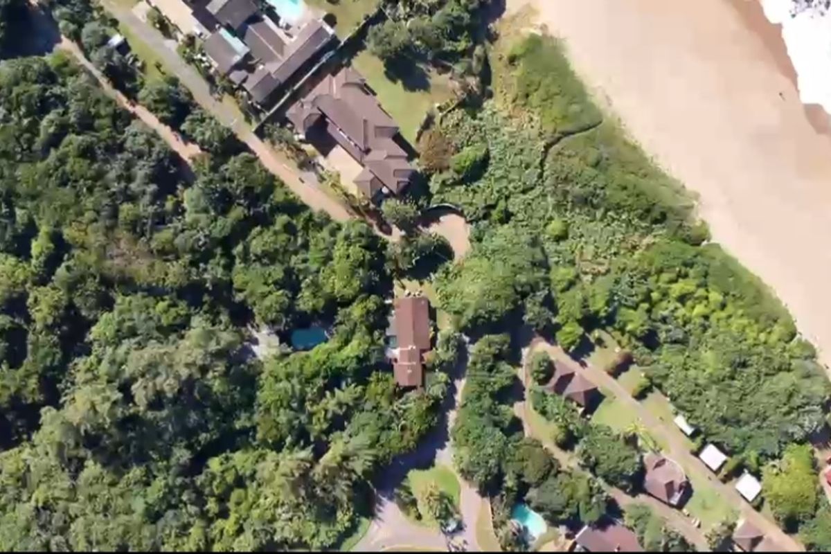 An aerial view of a coastal residential area surrounded by dense forest and beach access.
