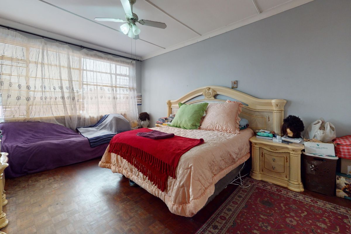 A spacious bedroom featuring parquet flooring, a ceiling fan, and a built-in wardrobe, offering a functional layout with potential for modernization.