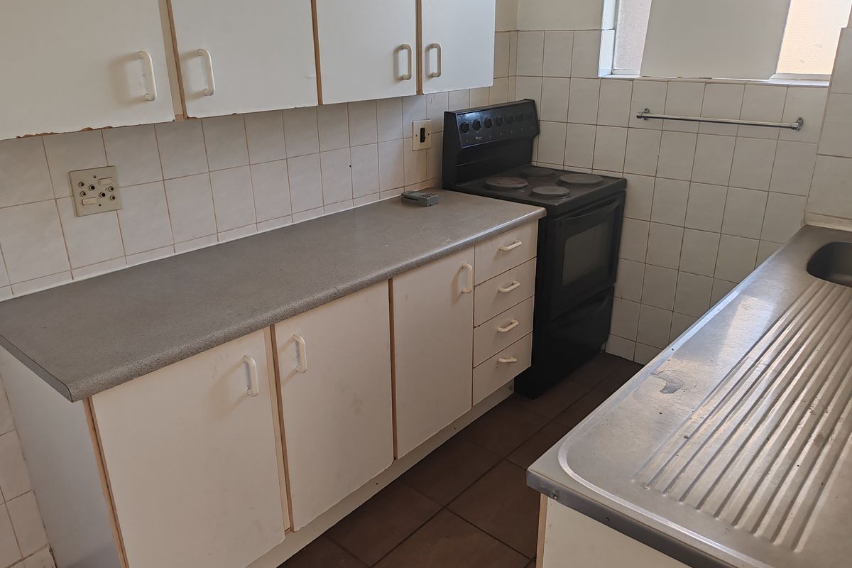A functional kitchen featuring white cabinetry, laminate countertops, a stainless steel sink, and a freestanding electric stove with tiled backsplash and flooring.