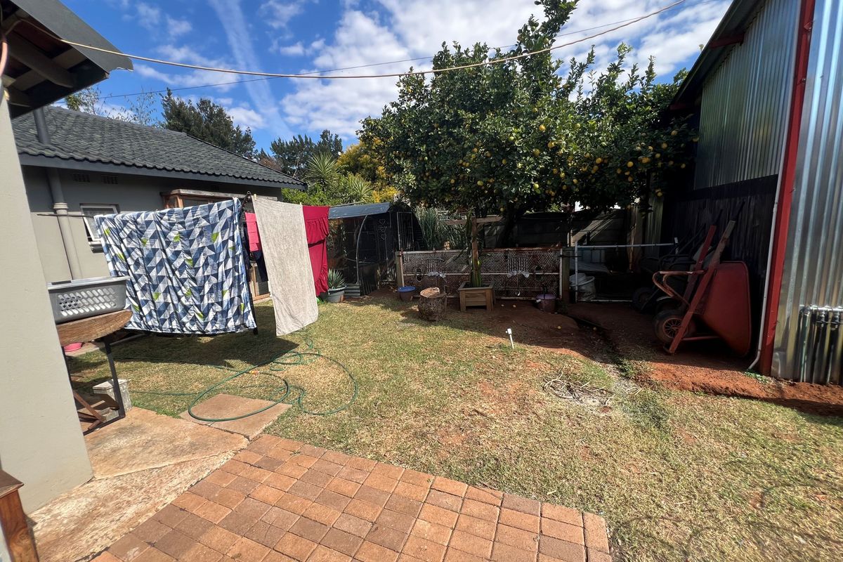 A rear garden area featuring a paved patio, lawn space, and corrugated metal structure, offering potential for landscaping and outdoor improvement.