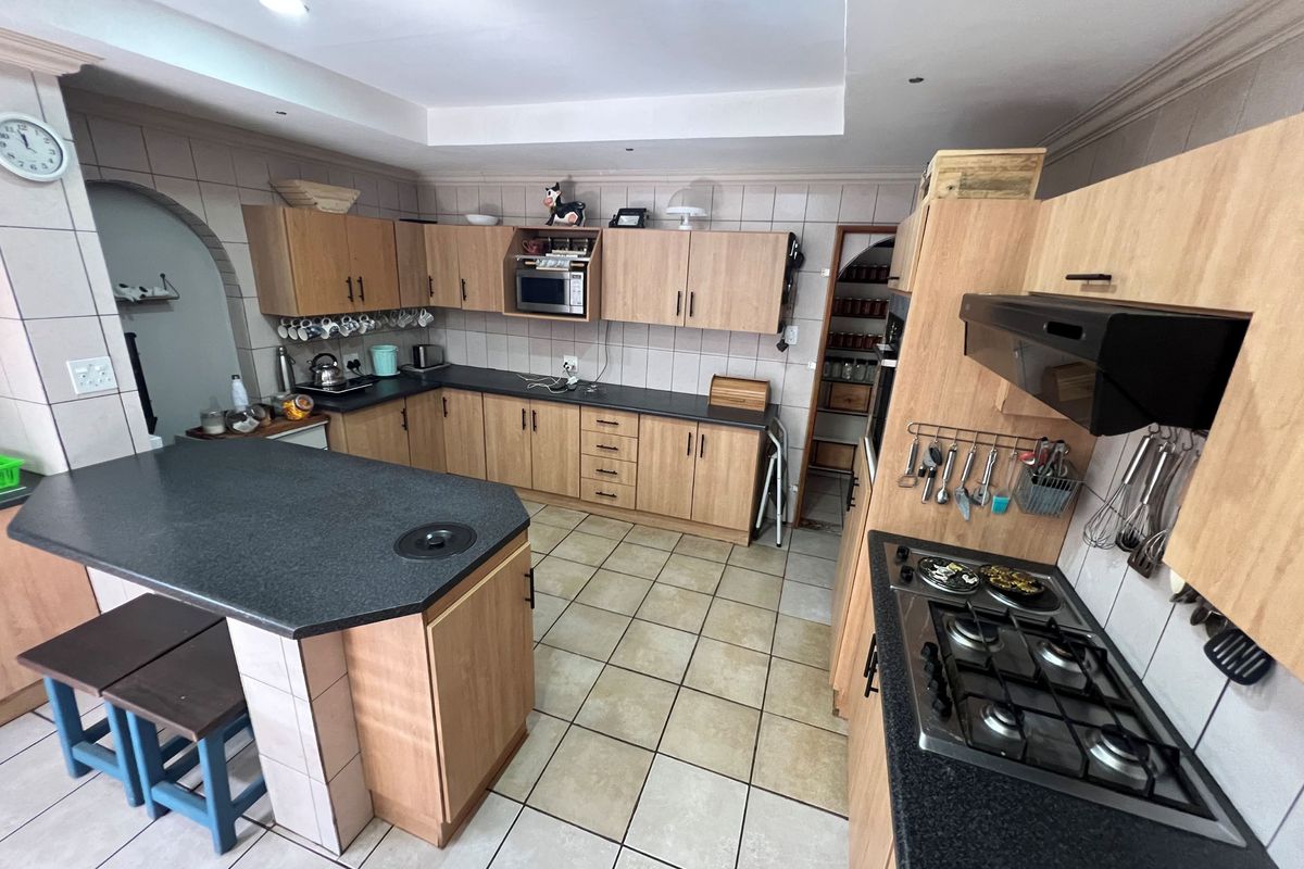 Spacious kitchen featuring wood-finish cabinetry, dark laminate countertops, a central island, gas hob, and integrated appliances with tiled flooring throughout.