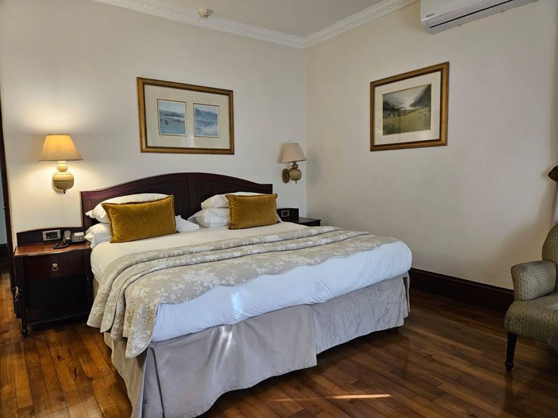 A well-maintained bedroom featuring polished hardwood flooring, crown molding, and a wall-mounted air conditioning unit.