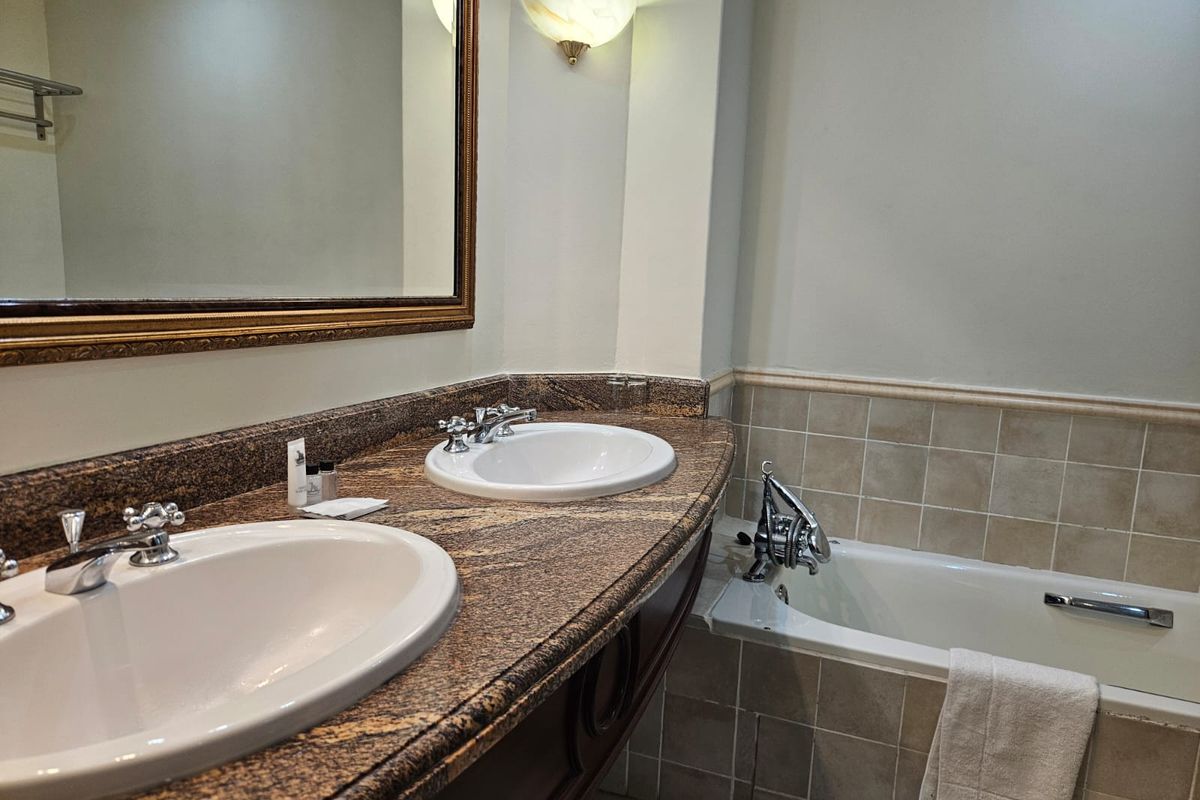 A functional bathroom featuring a double vanity with granite countertops, drop-in sinks, and a built-in bathtub with tiled surround.