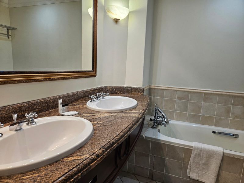 A functional bathroom featuring a double vanity with granite countertops, drop-in sinks, and a built-in bathtub with tiled surround.