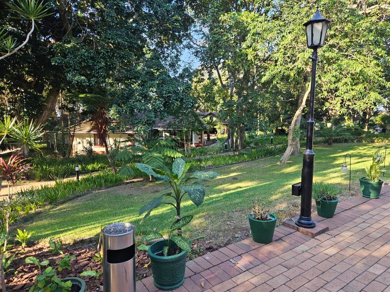 A well-maintained garden area featuring a paved walkway, mature trees, and a classic lamp post, providing a serene outdoor setting.