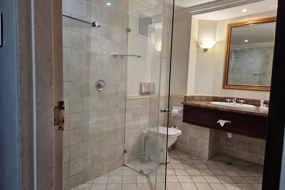A functional bathroom featuring a glass-enclosed shower, granite-topped vanity, and neutral tiled finishes, ready for a modern update.