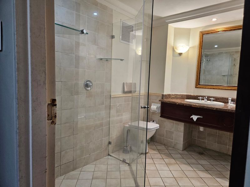 A functional bathroom featuring a glass-enclosed shower, granite-topped vanity, and neutral tiled finishes, ready for a modern update.