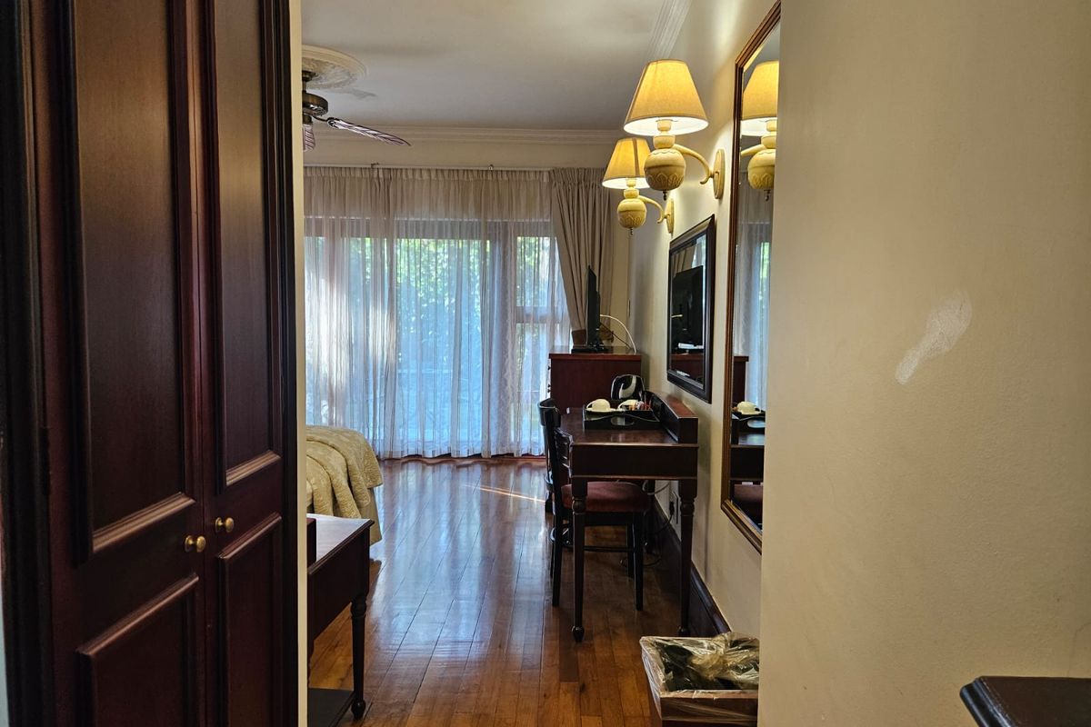 A bedroom featuring hardwood flooring, ceiling fan, and sliding glass doors leading to an outdoor area, with wall-mounted lighting and a large mirror.