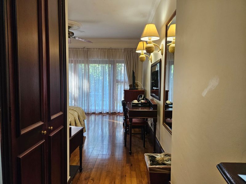 A bedroom featuring hardwood flooring, ceiling fan, and sliding glass doors leading to an outdoor area, with wall-mounted lighting and a large mirror.