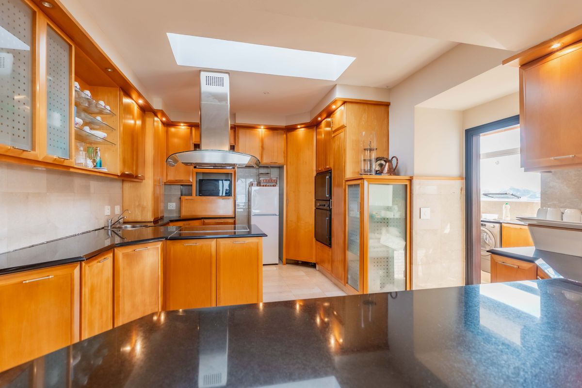 A well-appointed kitchen featuring warm wooden cabinetry, sleek black granite countertops, a central skylight, and integrated stainless steel appliances.