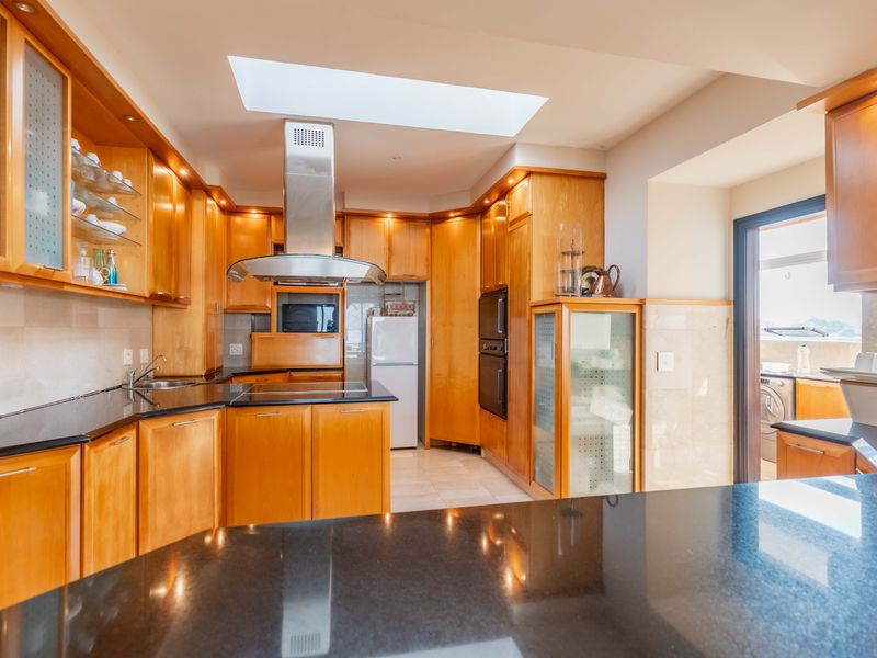 A well-appointed kitchen featuring warm wooden cabinetry, sleek black granite countertops, a central skylight, and integrated stainless steel appliances.