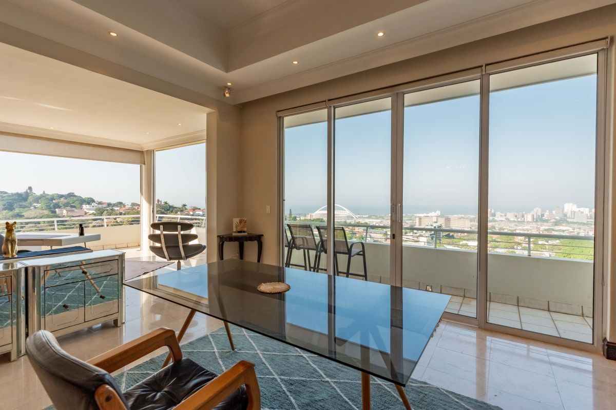 Spacious living area featuring a tray ceiling, recessed lighting, and large sliding glass doors that open onto a balcony with expansive city views.