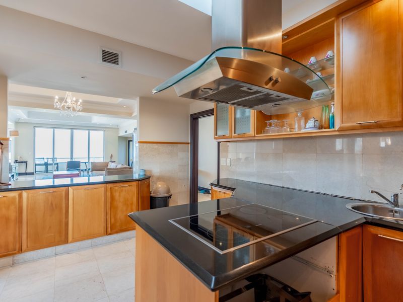 Open-plan kitchen featuring wooden cabinetry, black granite countertops, induction hob, and stainless steel extractor, flowing into a spacious living area with natural light.