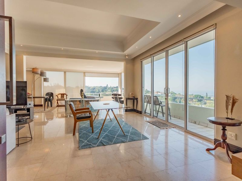 Spacious open-plan living area featuring high-quality marble flooring, recessed ceiling lighting, and expansive sliding glass doors leading to a private balcony with scenic views.