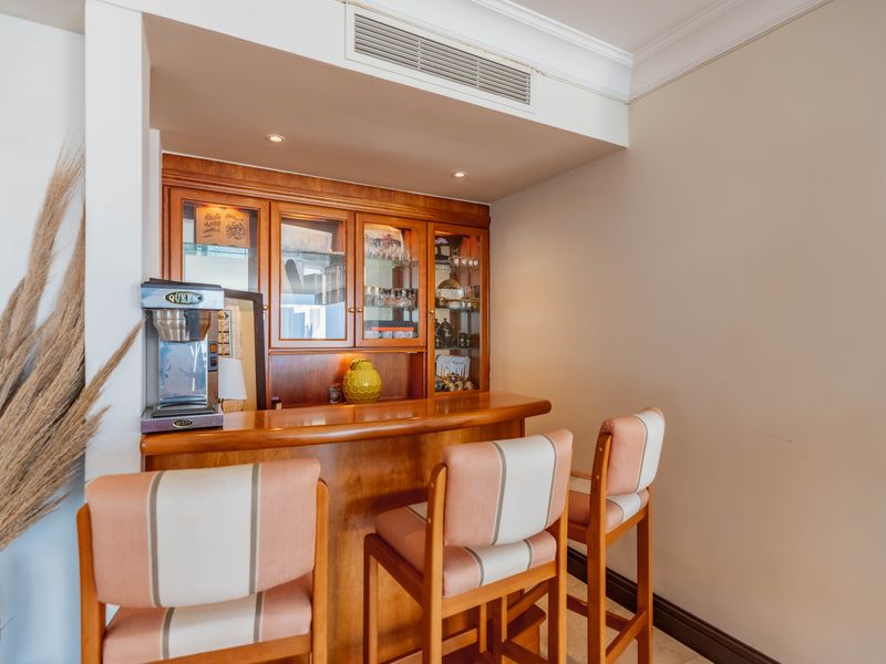 A dedicated bar area featuring built-in wooden cabinetry, glass display shelving, and a matching bar counter with integrated lighting and air conditioning.