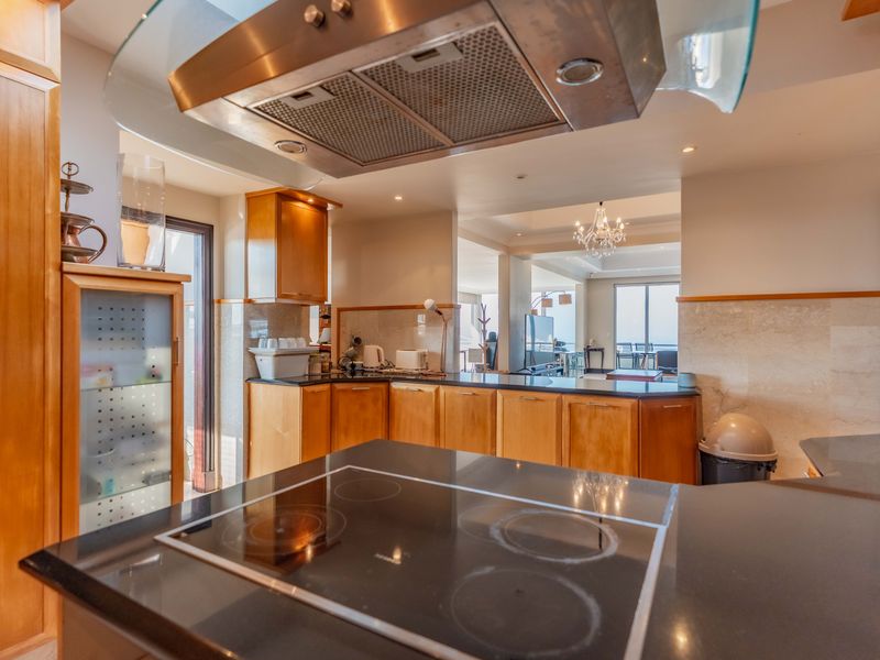 A well-appointed kitchen featuring warm wooden cabinetry, black granite countertops, a built-in electric hob, and a modern stainless steel extractor fan.