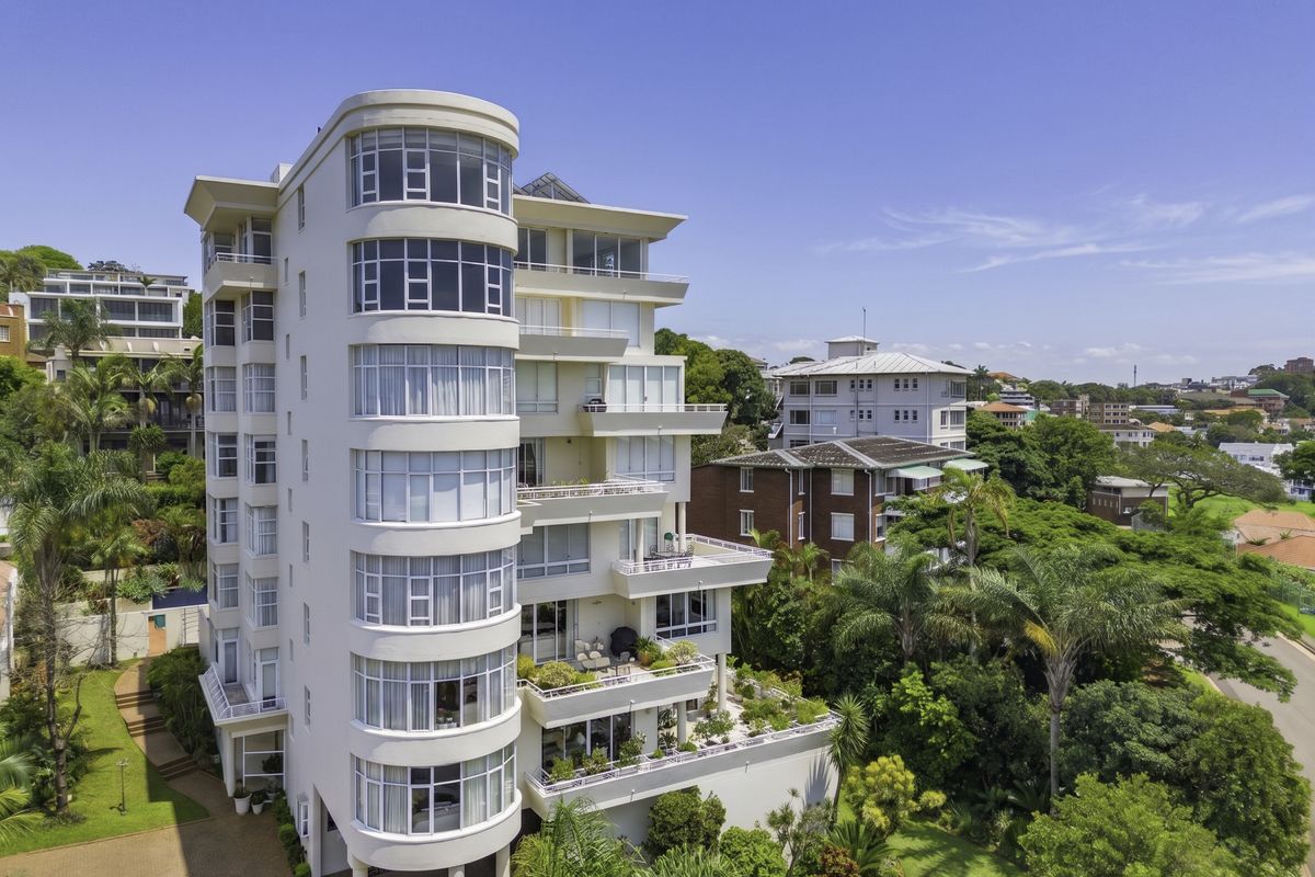 Aerial view of a modern multi-story penthouse building featuring curved architectural lines, expansive balconies, and well-maintained surrounding gardens.