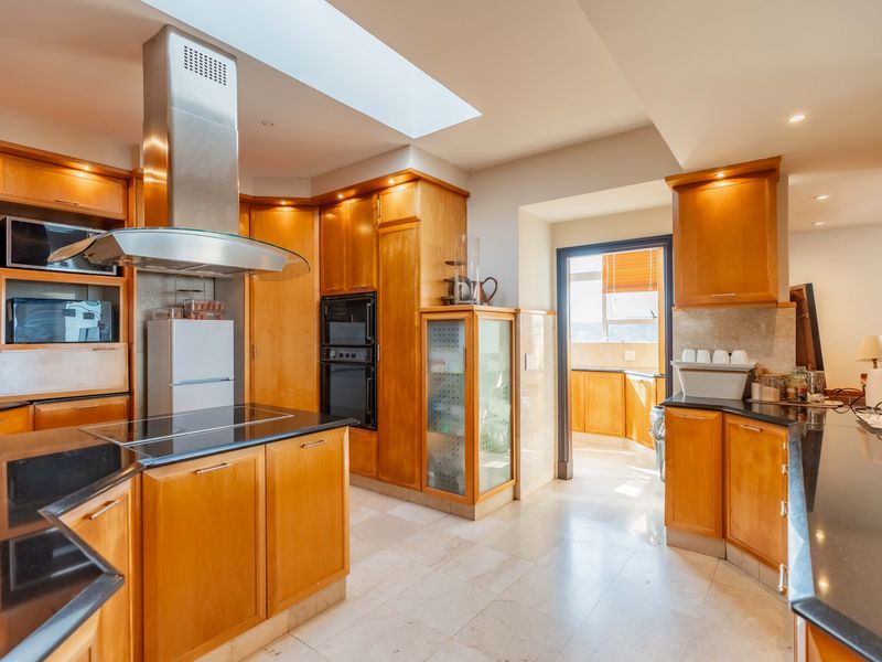 Spacious kitchen featuring warm wooden cabinetry, black granite countertops, integrated appliances, and a large skylight providing ample natural light.