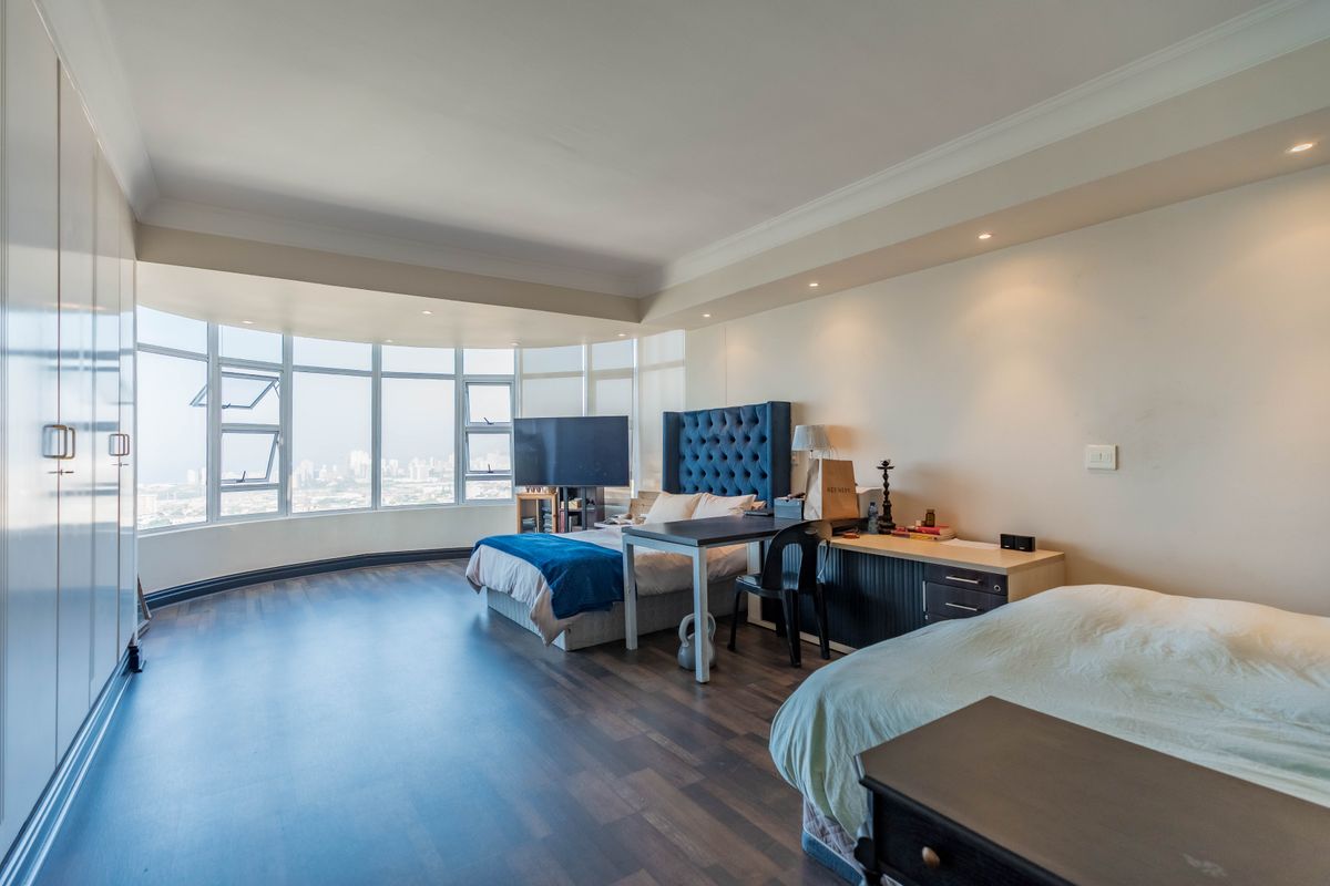 Spacious penthouse bedroom featuring large panoramic windows with city views, built-in cupboards, recessed lighting, and dark laminate flooring.