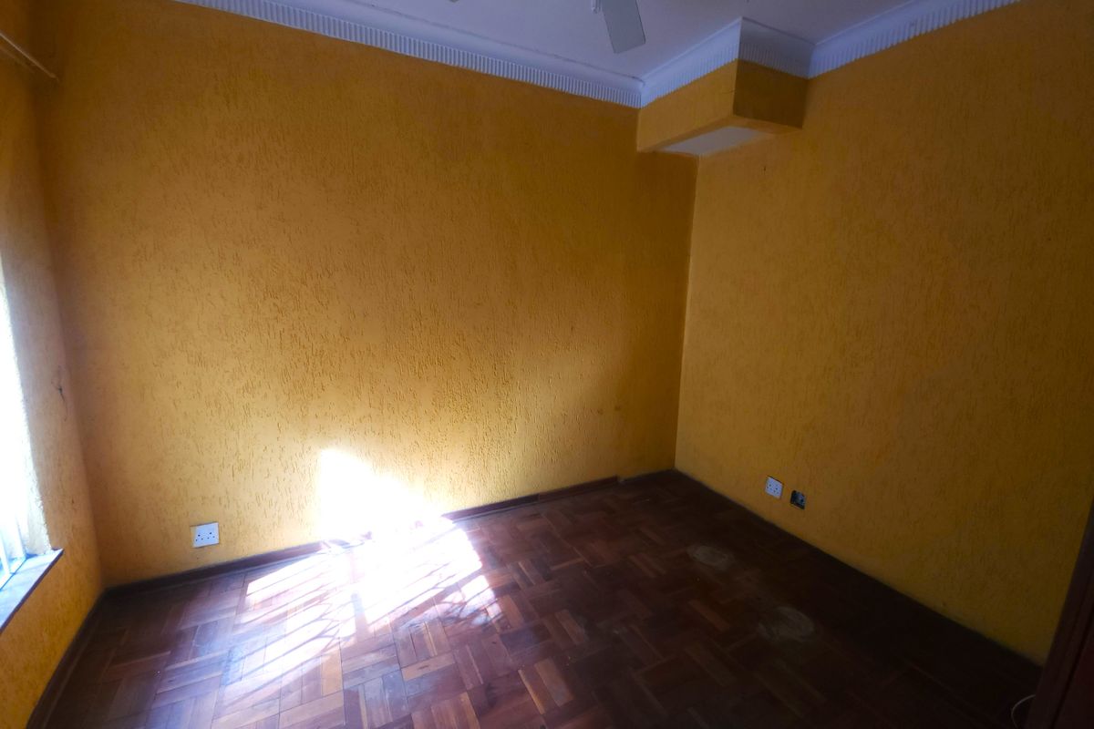 An empty bedroom featuring original parquet flooring, crown molding, and a ceiling fan, requiring cosmetic updates to the walls and floor finish.