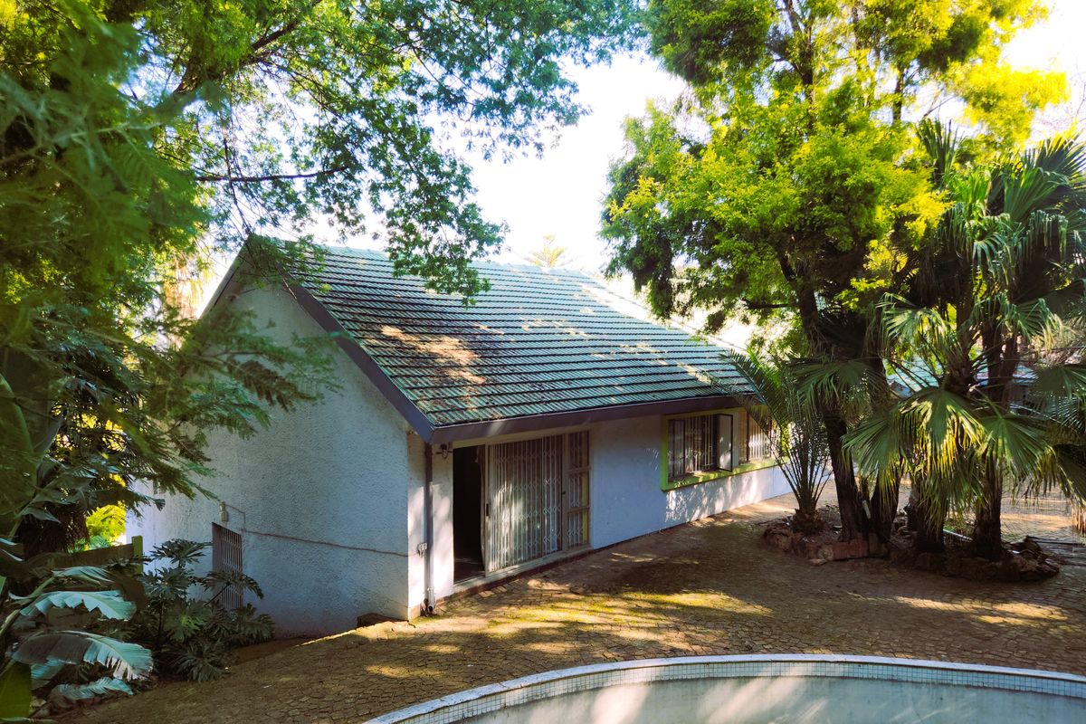 Rear view of the property featuring a tiled roof, sliding glass doors with security gates, and a paved courtyard area with a swimming pool.