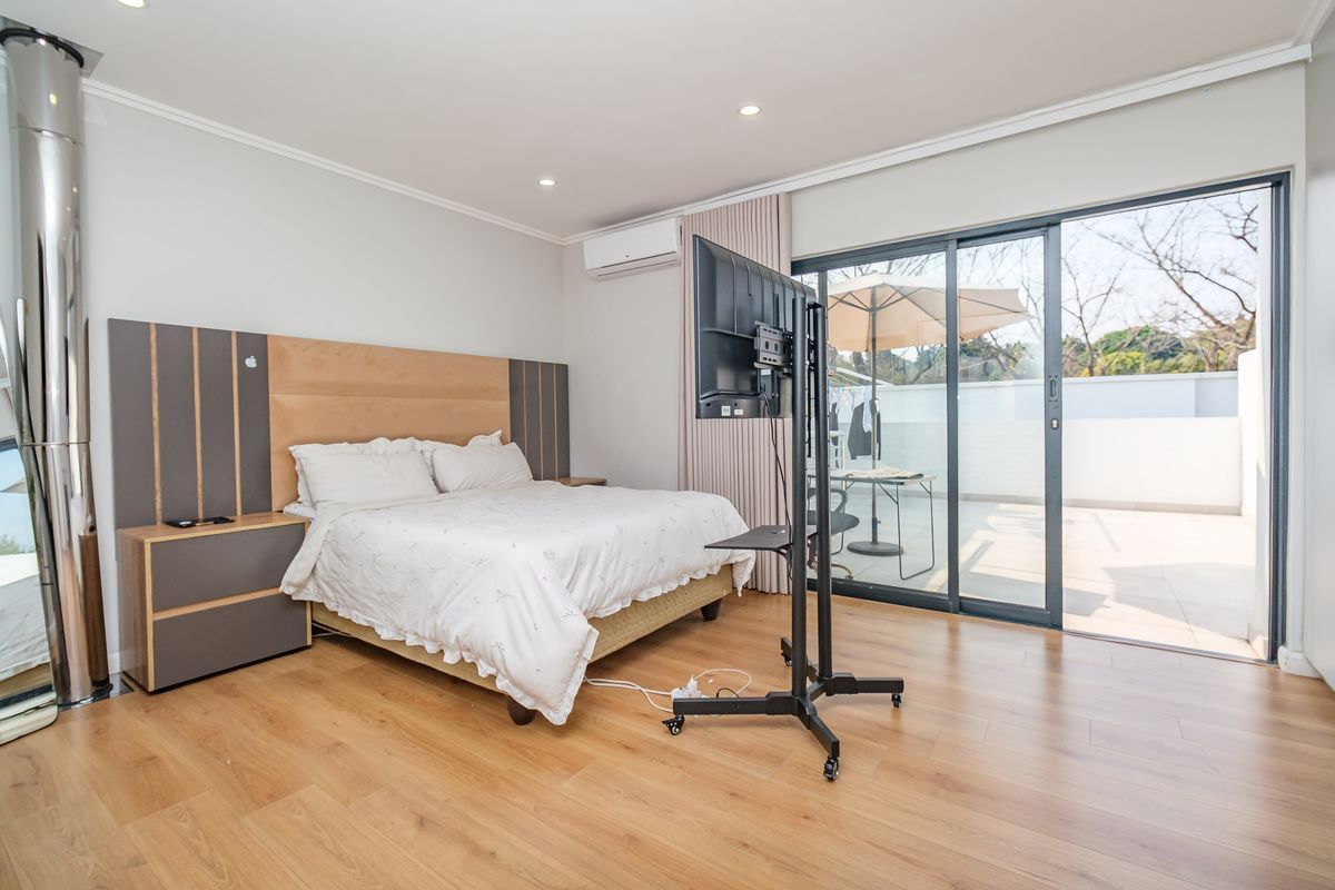 Spacious bedroom featuring laminate flooring, a built-in headboard, split-system air conditioning, and direct access to a private balcony through sliding glass doors.