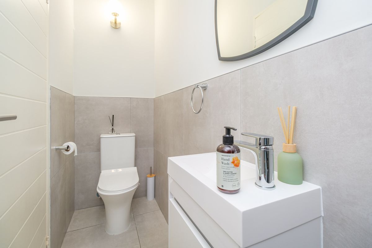 A modern, well-maintained guest bathroom featuring neutral grey wall tiles, a sleek vanity basin, and a wall-mounted toilet.