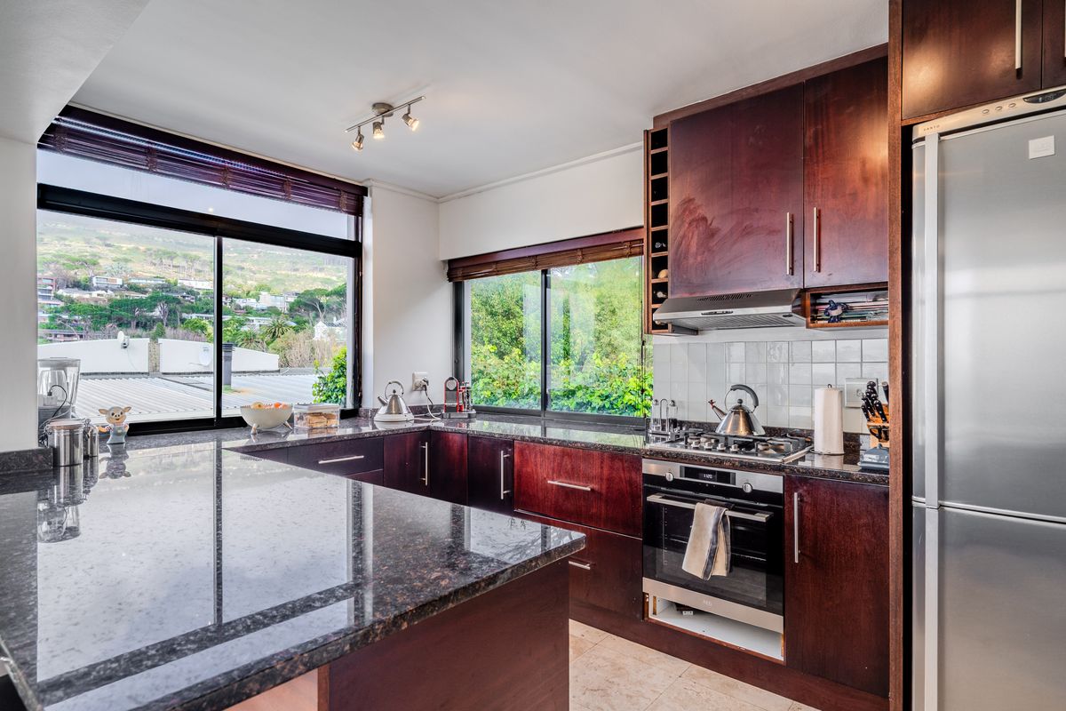 A functional kitchen featuring dark wood cabinetry, granite countertops, built-in oven, gas hob, and large windows offering scenic views.