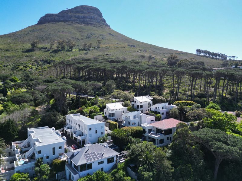 Aerial view of a residential estate nestled against a mountain backdrop, featuring multiple multi-story homes with varied roof styles and lush surrounding greenery.