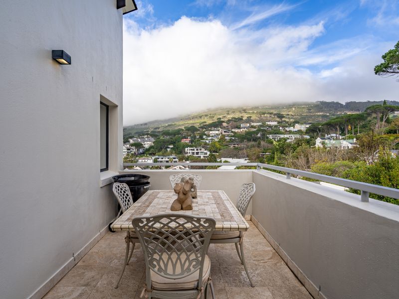 A spacious balcony featuring stone tile flooring, a metal safety railing, and an exterior wall light, offering scenic views of the surrounding landscape.