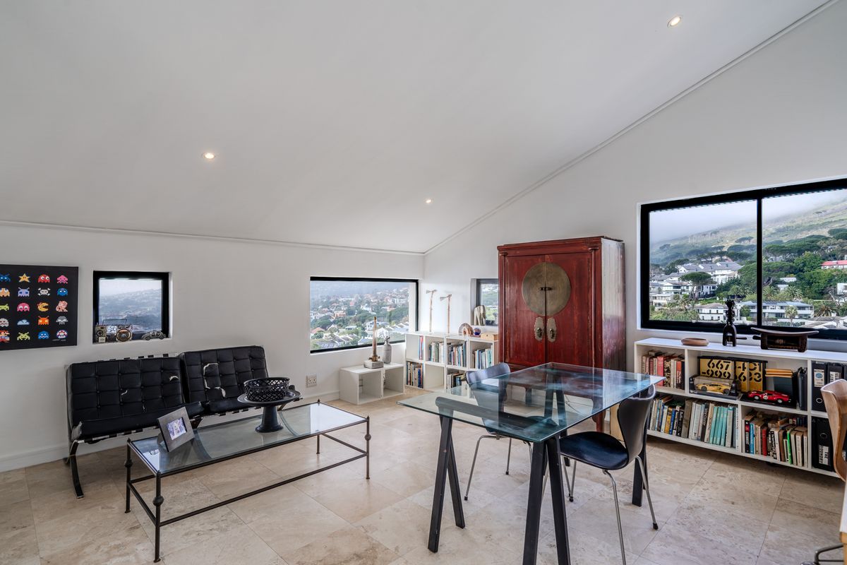 A bright living area featuring a sloped ceiling, recessed lighting, stone tile flooring, and large windows offering expansive views of the surrounding landscape.