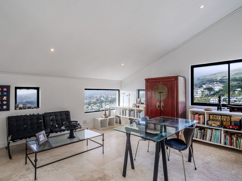 A bright living area featuring a sloped ceiling, recessed lighting, stone tile flooring, and large windows offering expansive views of the surrounding landscape.