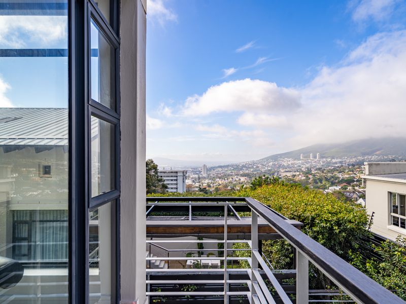 A modern balcony featuring a metal railing with a timber handrail, offering expansive elevated views of the surrounding cityscape and mountain landscape.