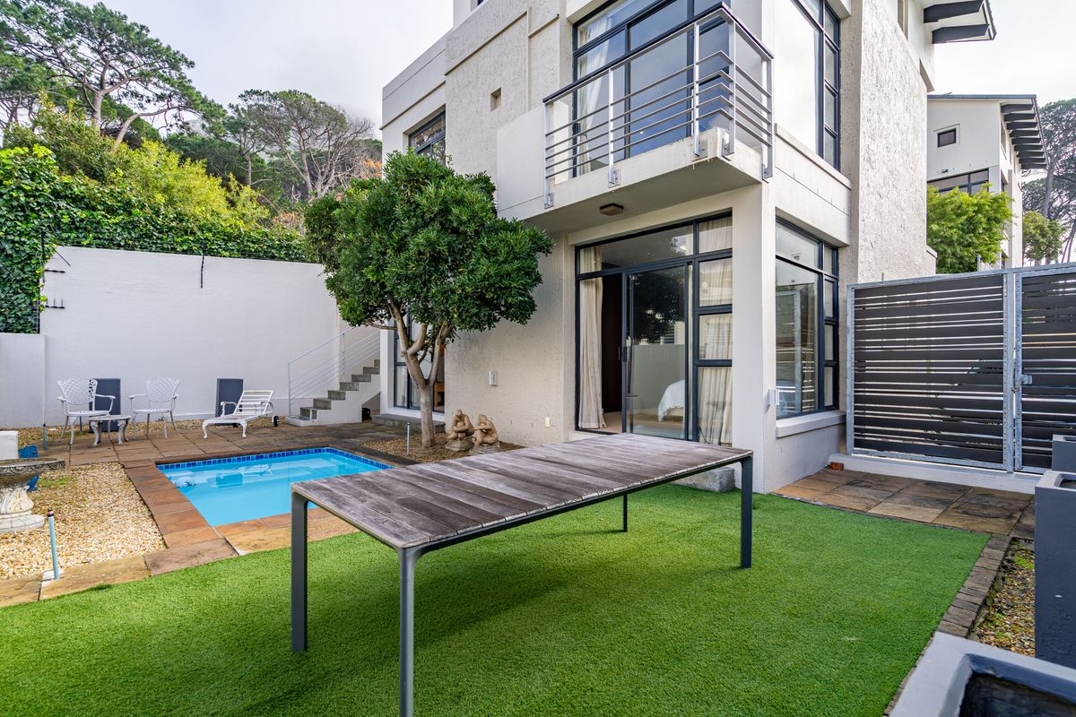 Rear exterior view featuring a private swimming pool, paved patio area, artificial lawn, and a balcony overlooking the garden.