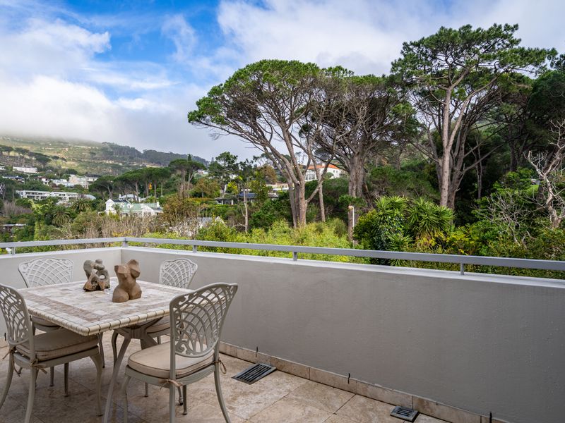 A spacious balcony featuring tiled flooring and a metal railing, offering scenic views of the surrounding trees and hillside landscape.