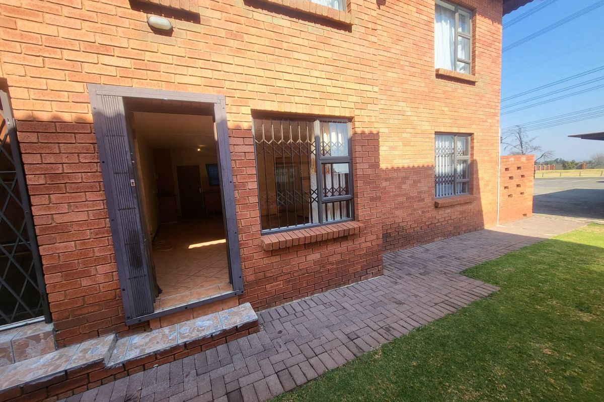 Rear view of a face brick townhouse featuring a paved walkway, security gates on windows and doors, and a small garden area.