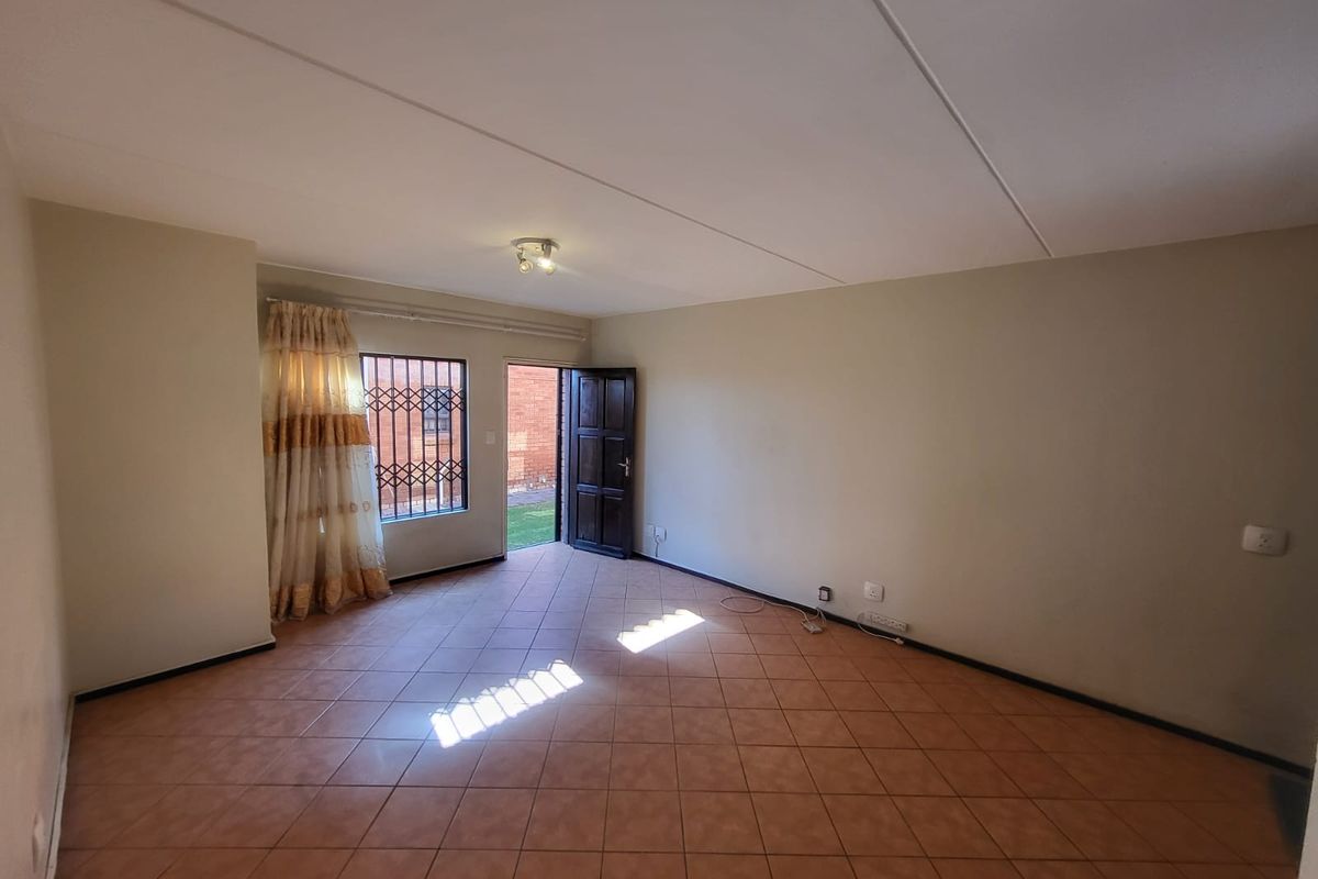 An empty, open-plan living area featuring tiled flooring, a security gate, and direct access to the exterior garden space.