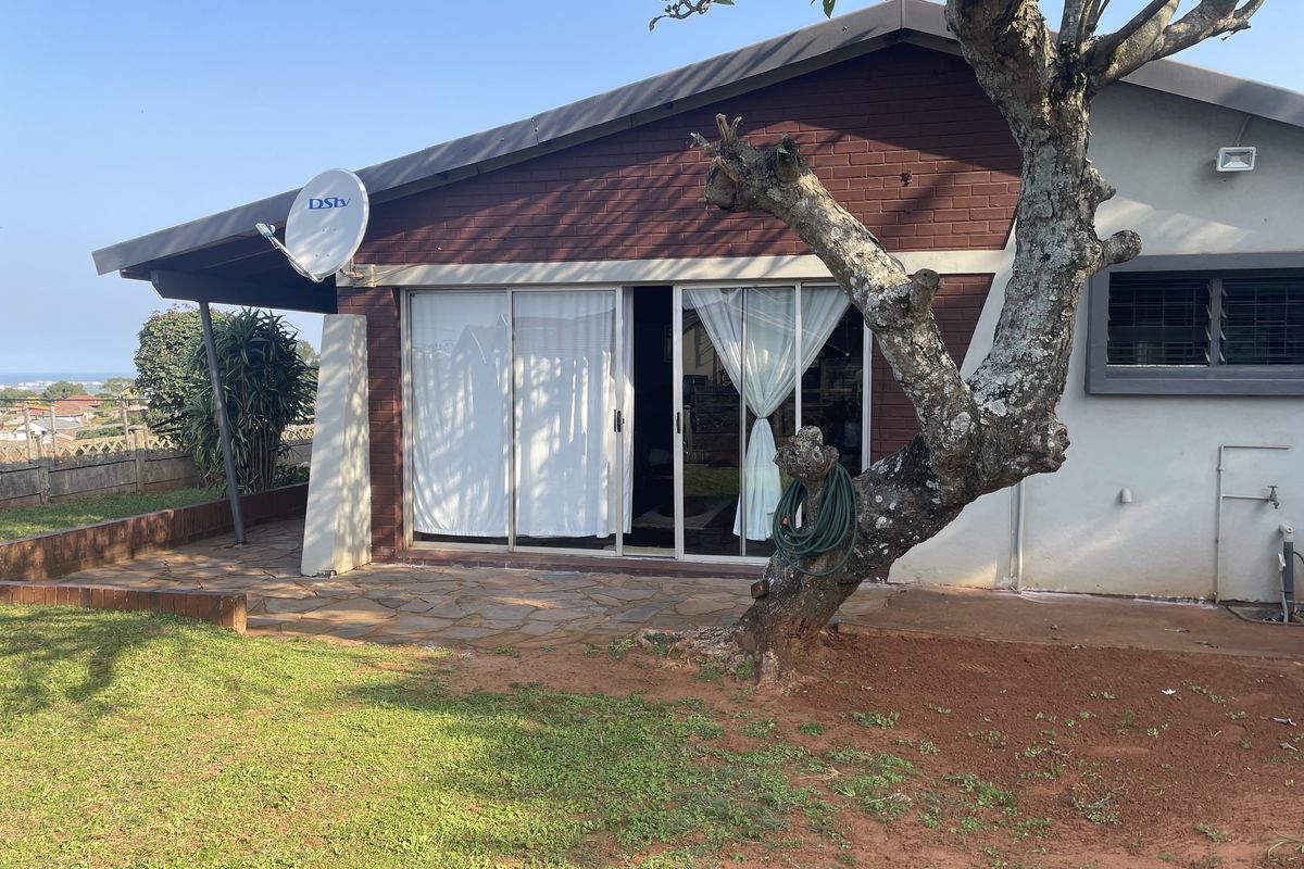 Rear exterior view of the house featuring a paved patio area, sliding glass doors, and a brick facade with a garden space.