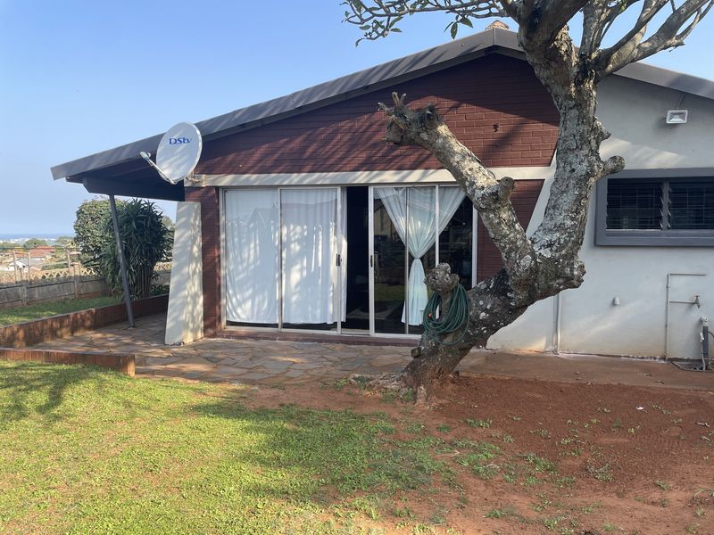 Rear exterior view of the house featuring a paved patio area, sliding glass doors, and a brick facade with a garden space.