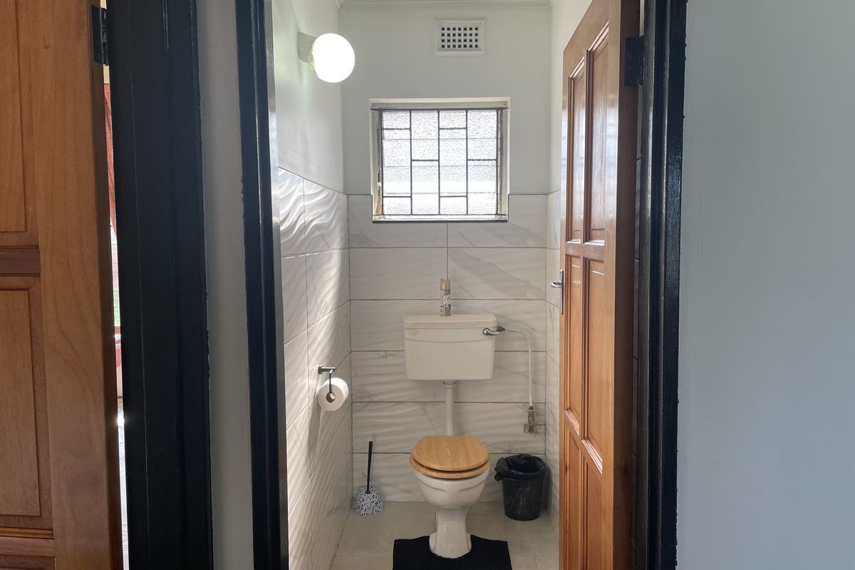 A compact, functional bathroom featuring modern white textured wall tiles, a standard toilet, and a security-grille window for ventilation.