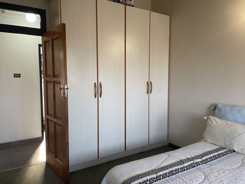 A bedroom featuring a large, light-toned built-in wardrobe with vertical wood trim and a solid timber door leading to an adjacent space.