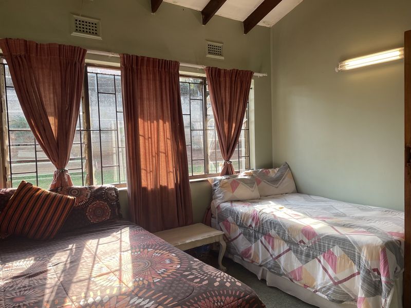 A bedroom featuring exposed timber ceiling beams, large windows with security bars, and a wall-mounted light fixture.