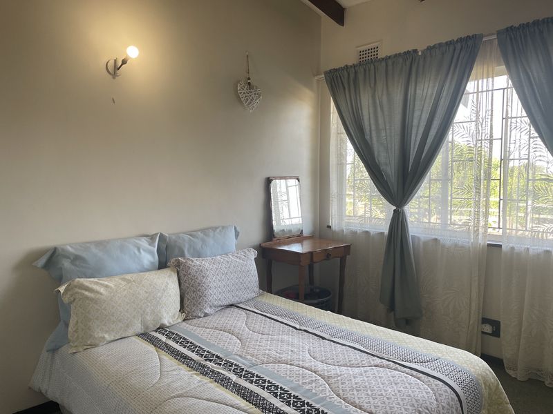 A bedroom featuring a window with security bars, a wall-mounted light fixture, and a ventilation grille.