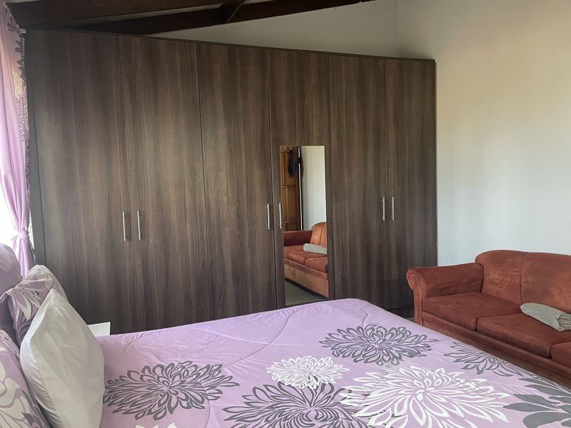 A bedroom featuring a large, dark wood-grain built-in wardrobe with a central mirror and exposed timber ceiling beams.