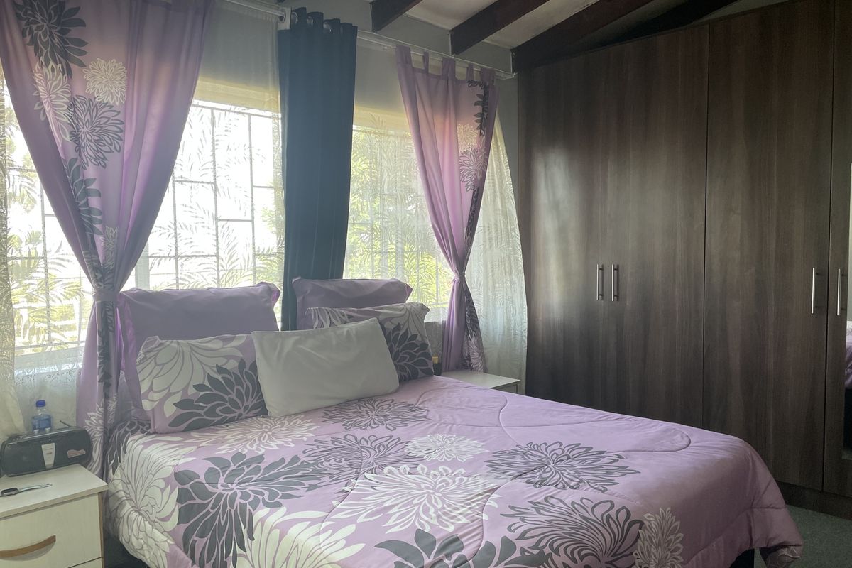 A well-maintained bedroom featuring exposed timber ceiling beams, large built-in wardrobes, and windows fitted with security bars.