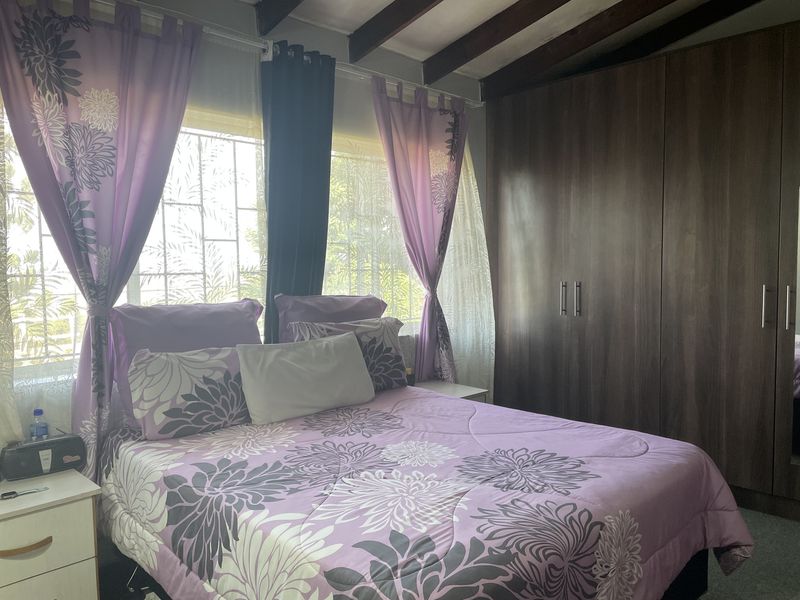 A well-maintained bedroom featuring exposed timber ceiling beams, large built-in wardrobes, and windows fitted with security bars.