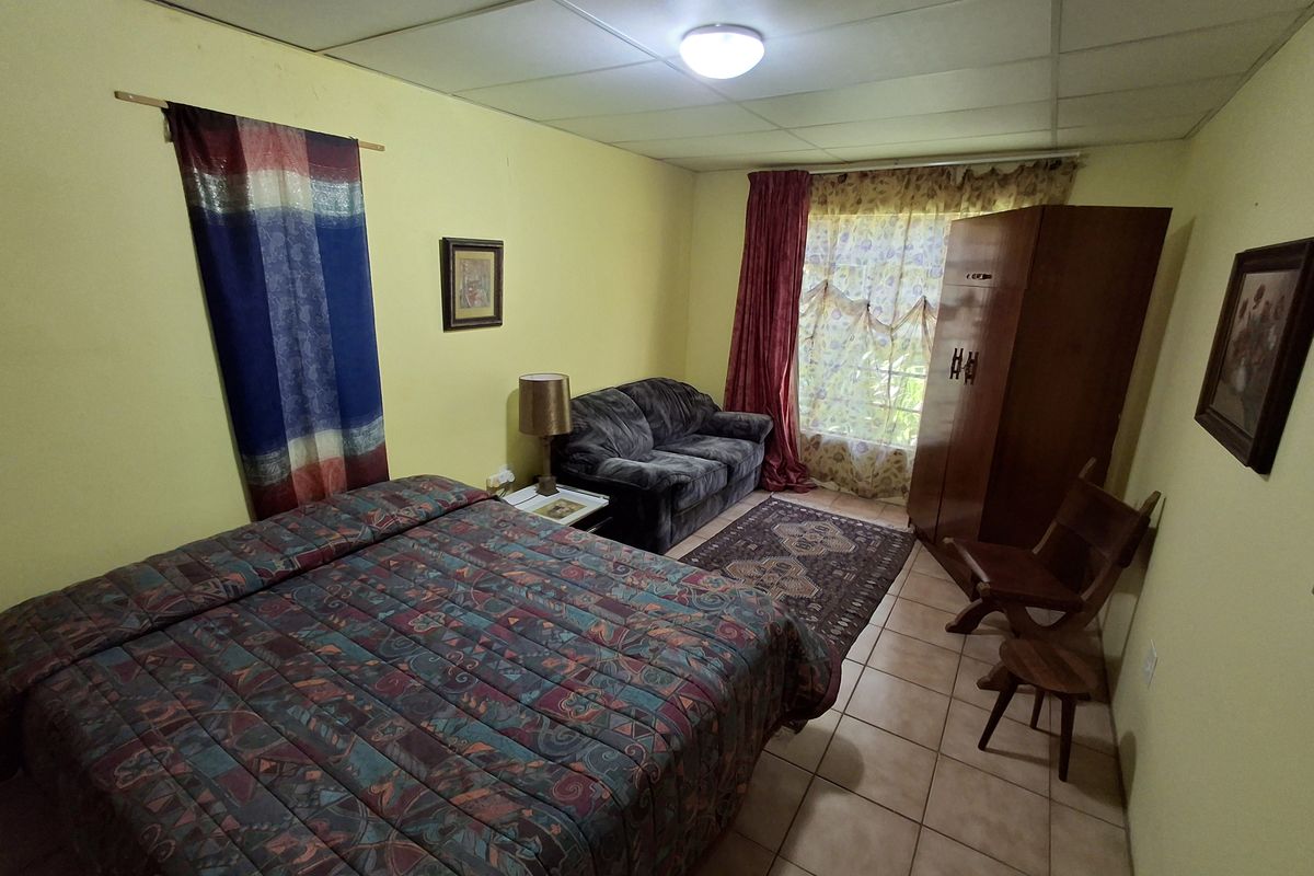 A bedroom featuring tiled flooring and a drop ceiling, currently furnished with a bed and wardrobe.