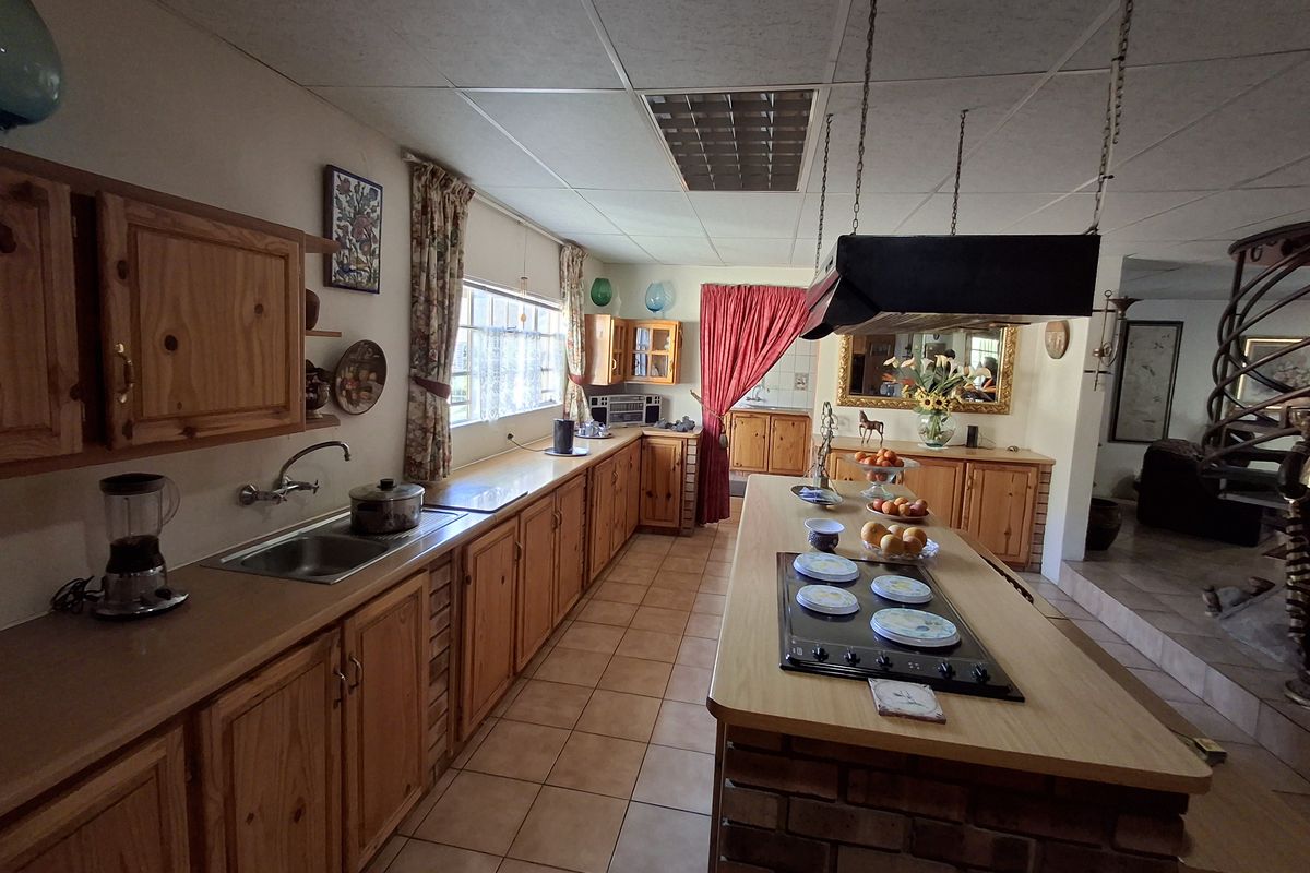 Spacious kitchen featuring extensive wooden cabinetry, a central island with a built-in hob, and tiled flooring, offering significant potential for modern renovation.
