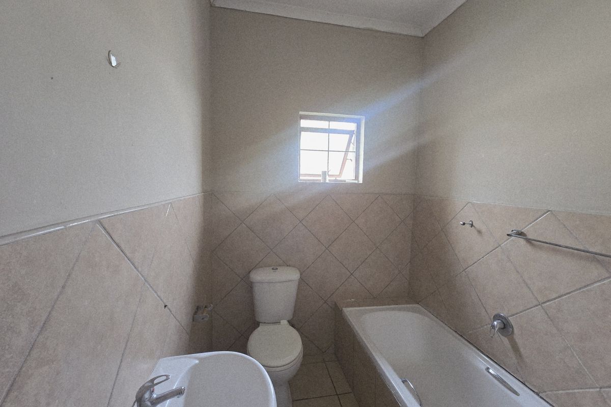 A functional bathroom featuring a bathtub, pedestal basin, and toilet with neutral tiled walls and flooring, awaiting personal touches.